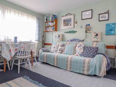 A living room with a sofa covered in striped fabric and sea-themed pillows beside a dining table with chairs and a patterned tablecloth at Villa 29 in Camelford