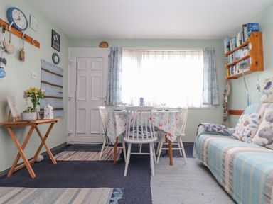 A dining area with a table and chairs by a window next to a sofa with cushions and a wooden side table with plants at Villa 29 in Camelford