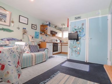 A small living area and kitchen with a striped sofa and mounted TV at Villa 29 in Camelford