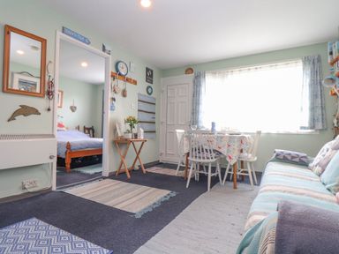 A small living and dining area with a table and chairs next to a window and a striped sofa with cushions in Villa 29 Camelford
