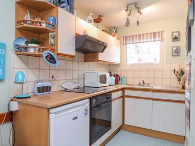 A small kitchen with wooden countertops white cabinets a stove oven microwave sink and a window with a striped blind at Villa 29 in Camelford