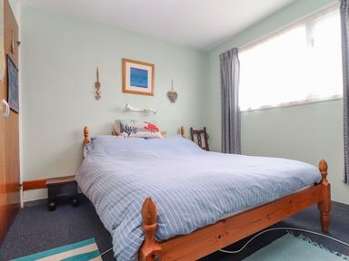 A bedroom with a wooden bed with blue striped bedding a window with curtains and wall decorations at Villa 29 in Camelford