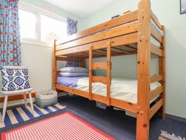 A bedroom with wooden bunk beds a chair with pillow a striped rug and a basket under a window at Villa 29 in Camelford