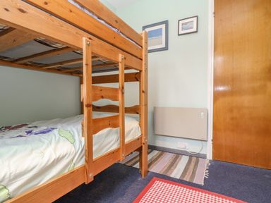 A bedroom with wooden bunk beds a door two framed pictures and two rugs on the floor at Villa 29 in Camelford