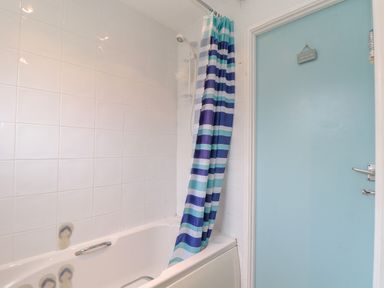 A bathroom with a white bathtub with grab bars blue and white striped shower curtain and a blue door at Villa 29 in Camelford