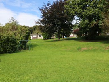 A grassy outdoor area with trees swings and houses in the background at Villa 29 in Camelford
