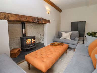 A living room with a wood burning stove gray sofas and an orange ottoman at Lynton Cottage in Enstone