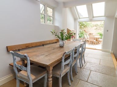 A dining room with a wooden table and chairs opening to an outdoor patio at Lynton Cottage in Enstone