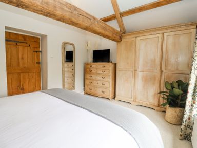 A bedroom with a wooden door a chest of drawers a wardrobe a full length mirror and a plant at Lynton Cottage in Enstone