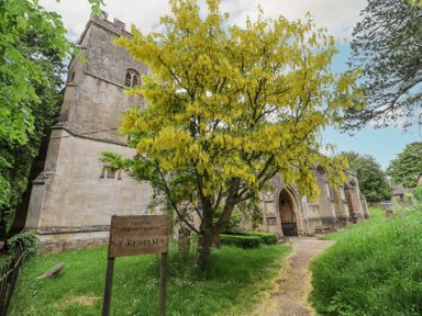 An old stone church with a yellow flowering tree and a wooden sign reading Enstone Parish Church St Kenelms
