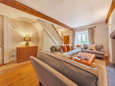 A living room with sofas orange cushions and a window at Lynton Cottage in Enstone