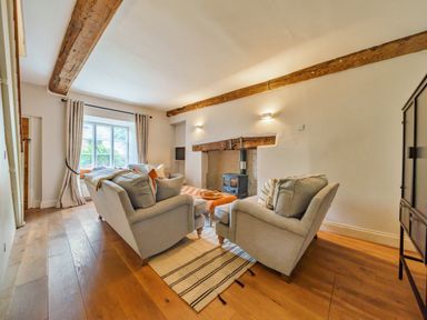 A living room with two armchairs a sofa a window with curtains and exposed wooden beams at Lynton Cottage in Enstone
