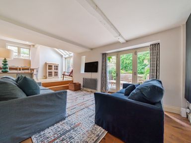 A living room with two sofas facing a wall-mounted TV and glass doors opening to a garden at Lynton Cottage in Enstone