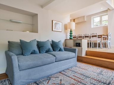 A living room with a blue sofa pillows a lamp and a dining area with a wooden table and chairs at Lynton Cottage in Enstone