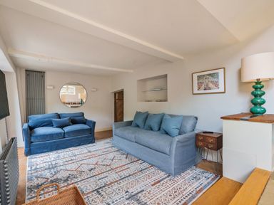A living room with two sofas a patterned rug a round mirror and a lamp at Lynton Cottage in Enstone
