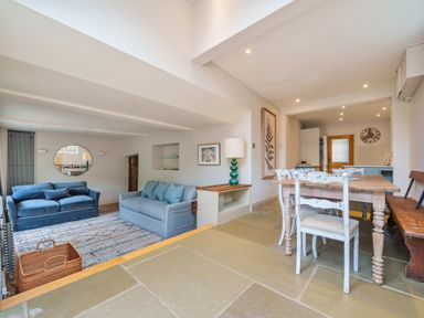 A living room with two sofas and a rug next to a dining area with a wooden table and chairs at Lynton Cottage in Enstone