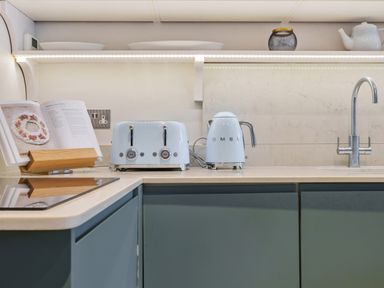 A kitchen countertop with a toaster kettle cooktop cookbook and sink at Lynton Cottage in Enstone