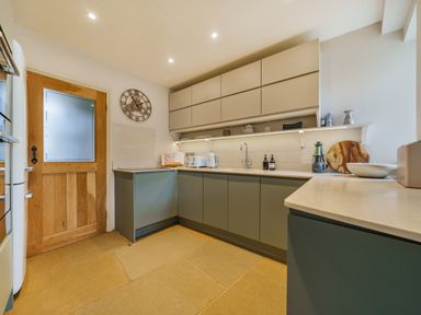 A kitchen with green lower cabinets and beige upper cabinets with a wooden door at Lynton Cottage in Enstone