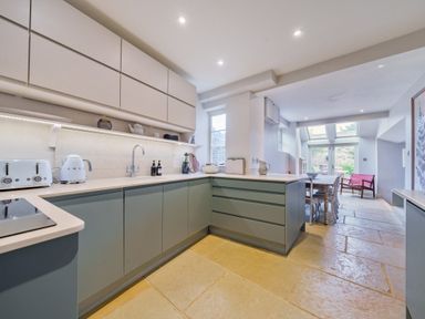 A kitchen with blue lower cabinets white upper cabinets and stone tile flooring at Lynton Cottage in Enstone