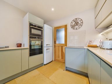 A kitchen with built in ovens a white fridge a wooden door and cupboards at Lynton Cottage in Enstone