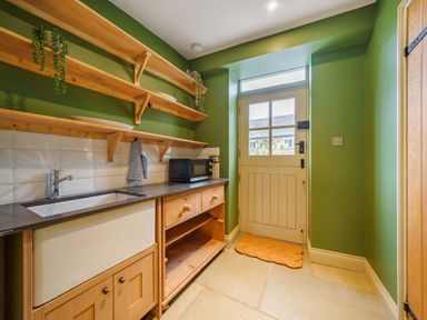 A kitchen with wooden shelves a sink a microwave and a door with a window at Lynton Cottage in Enstone