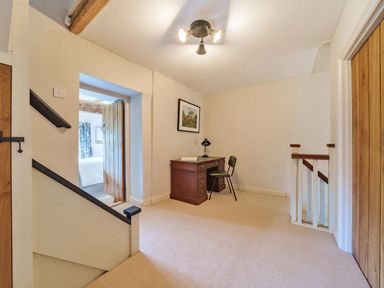 A hallway with a wooden desk and chair a framed picture on the wall and a door leading to a bedroom at Lynton Cottage in Enstone