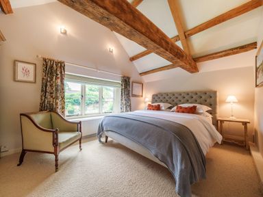 A bedroom with a bed a chair wooden beams and a window at Lynton Cottage in Enstone