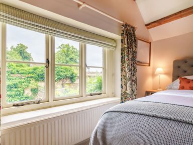 A bedroom with a bed near a window overlooking a garden at Lynton Cottage in Enstone