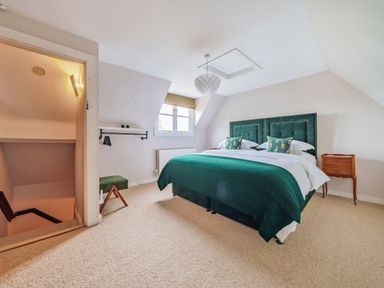 A bedroom with a green bedspread and pillows a wooden side table a window stairs and a small green stool at Lynton Cottage in Enstone