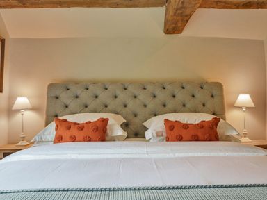 A bed with a tufted headboard two orange pillows white bedding and bedside lamps at Lynton Cottage in Enstone