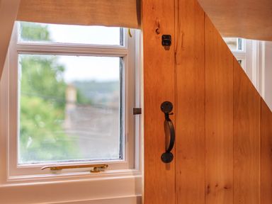 A window with a beige curtain next to a wooden door with a black handle at Lynton Cottage in Enstone