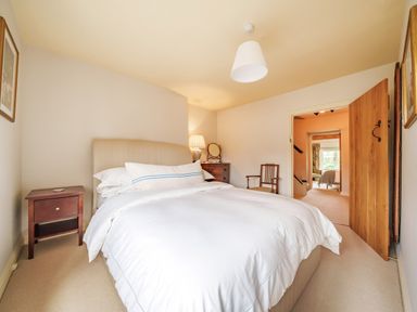 A bedroom with a bed a nightstand a chair and a dresser with a lamp at Lynton Cottage in Enstone