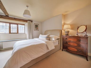 A bedroom with a bed beside a wooden dresser with a lamp and mirror at Lynton Cottage in Enstone