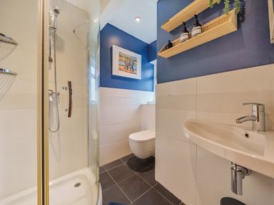 A bathroom with a shower enclosure a wall-mounted toilet a sink and shelves with bottles at Lynton Cottage in Enstone