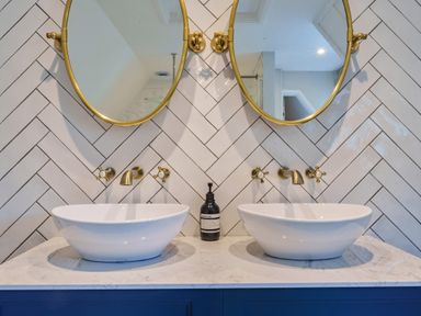 A bathroom vanity with two sinks round mirrors and brass fixtures at Lynton Cottage in Enstone