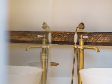 A brass faucet with white handles next to a white sink and a wooden beam on a wall at Lynton Cottage in Enstone