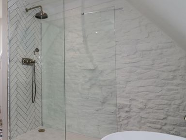 A bathroom shower area with glass partition stone textured wall and patterned tiles at Lynton Cottage in Enstone