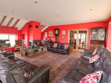A living room with red walls brown leather sofas a fireplace and wooden furniture at Cringoed House Llanarth near Aberaeron