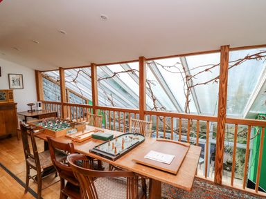A room with a wooden table and chairs with board games and foosball beside large slanted windows at Cringoed House Llanarth near Aberaeron
