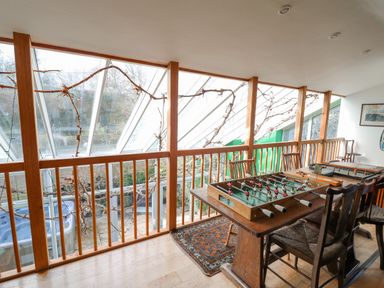 A room with a foosball table and wooden chairs next to a glass wall with wooden railings at Cringoed House Llanarth near Aberaeron