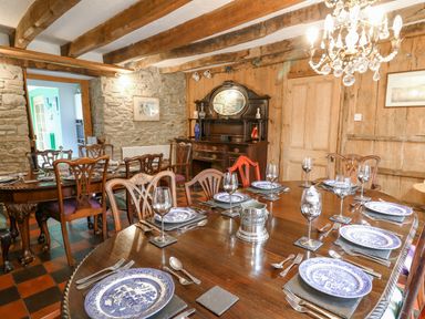 A dining room with wooden tables and chairs set with plates and wine glasses at Cringoed House Llanarth near Aberaeron
