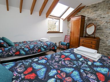 A bedroom with two single beds with butterfly bedspreads a wooden wardrobe a chest of drawers with a round mirror and an armchair at Cringoed House Llanarth near Aberaeron
