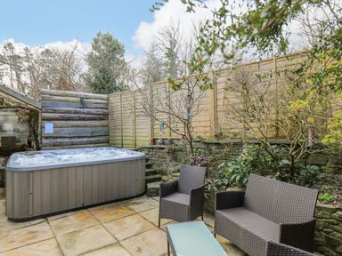 An outdoor patio with a hot tub a glass table a wicker chair and sofa surrounded by a wooden fence and plants at Cringoed House Llanarth near Aberaeron