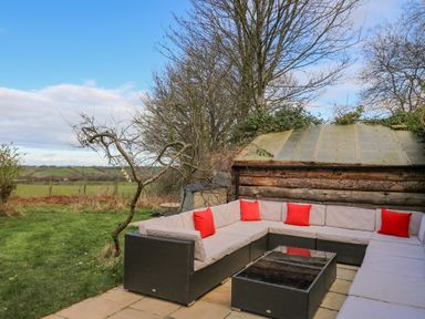 An outdoor seating area with a wicker sofa with red cushions and a glass coffee table near a wooden shed at Cringoed House Llanarth near Aberaeron