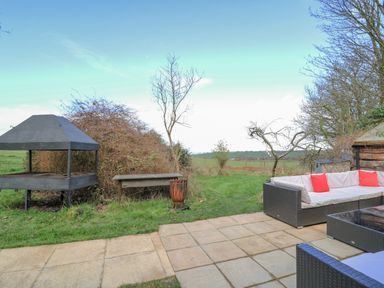 An outdoor patio with a wicker sofa and glass table near a grassy area with a fire pit and barbecue grill at Cringoed House Llanarth near Aberaeron