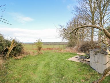 A grassy backyard area with trees and shrubs overlooking open fields at Cringoed House in Llanarth near Aberaeron