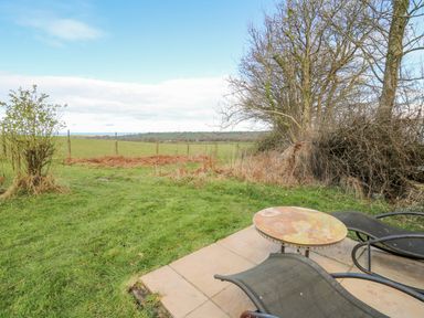 An outdoor patio area with two chairs and a round table facing a grassy field and trees at Cringoed House in Llanarth near Aberaeron