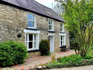 Stone house with white framed windows and a tiled patio with plants and a wooden bench at Cringoed House Llanarth near Aberaeron