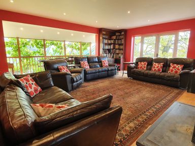 A living room with leather sofas and bookshelves near large windows at Cringoed House Llanarth near Aberaeron