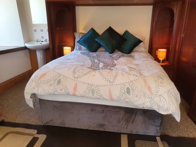A bed with patterned bedding and three pillows in a room with built-in wooden shelves and a sink at Cringoed House Llanarth near Aberaeron